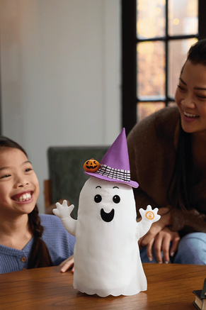 Ghost plush with witch hat on a table with mother and child playing with it.