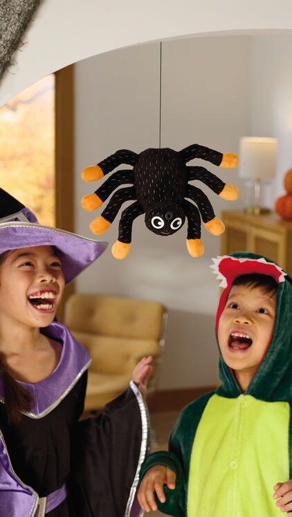 Children in costumes playing with a plush spider that hangs from the ceiling.